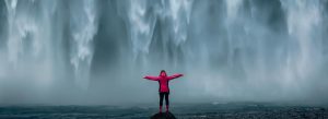Iceland geography school trip with a student in a red coat stood under Skogafoss waterfall