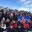 A geography school group posing in snowy conditions at Þingvellir National Park in Iceland, holding the Icelandic flag, with snow-covered volcanic rock formations and clear blue sky in the background.