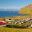 Panoramic view of the coastal village of Vík í Mýrdal in South Iceland, showing the iconic Reynisdrangar sea stacks, basalt cliffs, and red-roofed church — a picturesque stop on geography school trips focused on coastal erosion and volcanic landscapes.