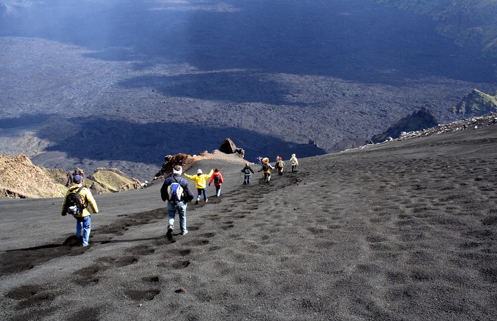 Geography school trip hikers descend volcanic ash slopes from the summit of Mount Etna