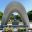 Peace memorial monument with stone arch and flowers in foreground, with Atomic Bomb Dome and reflection pool in Hiroshima Peace Memorial Park, Japan, on a school history trip.