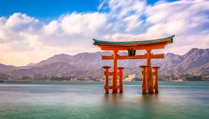 Iconic floating Torii gate of Itsukushima Shrine in Miyajima, Japan with calm water and mountain backdrop, popular destination for cultural and educational school trips.